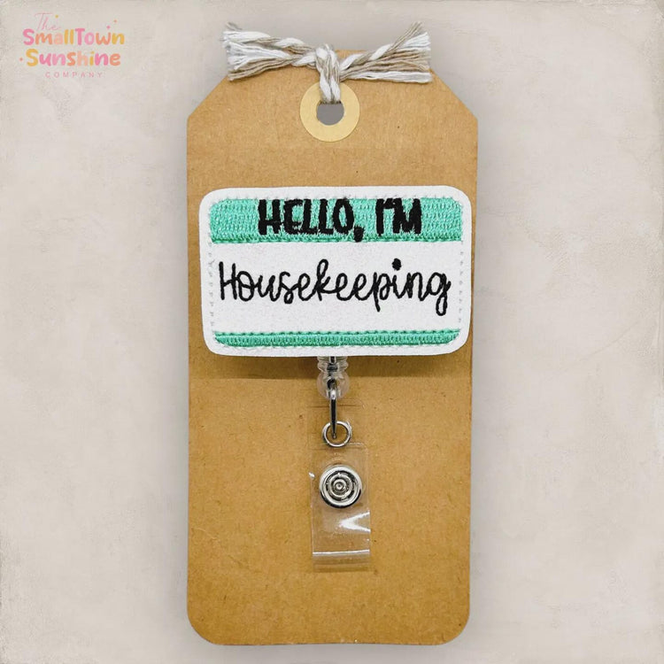 a brown paper tag with a green and white embroidered name tag attached to it. The name tag says "Hello, I'm Housekeeping".