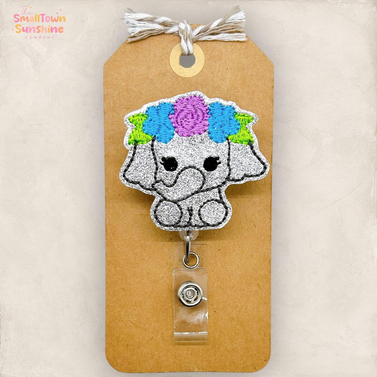 a small, glittery elephant-shaped badge with a floral headpiece attached to a brown paper tag.
