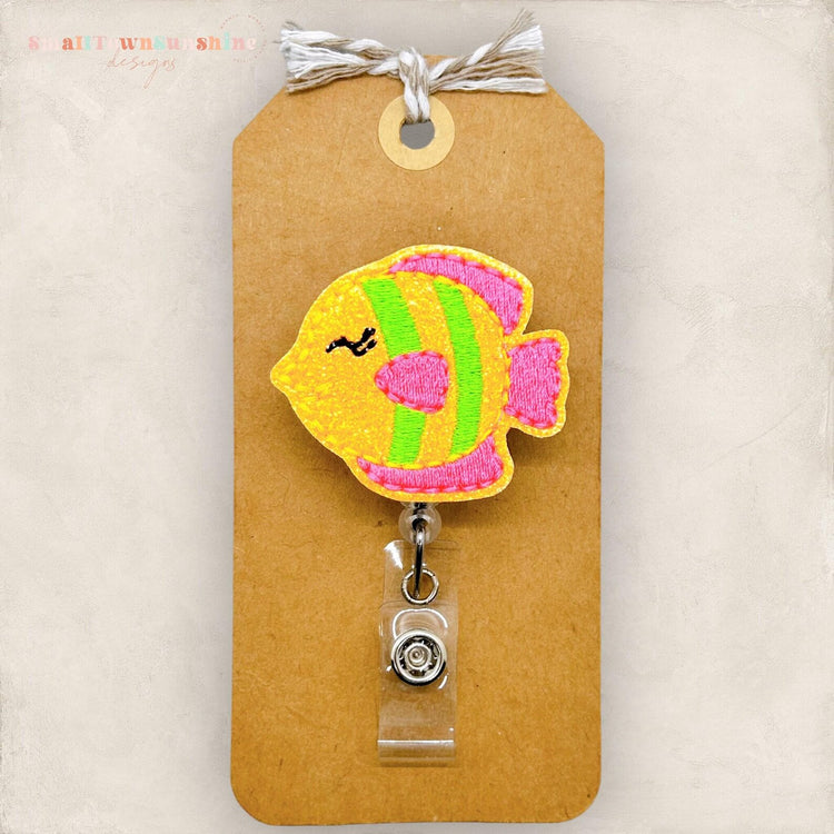 A colorful, hand-stitched fish-shaped badge or lanyard with a clear plastic tag attached to it.