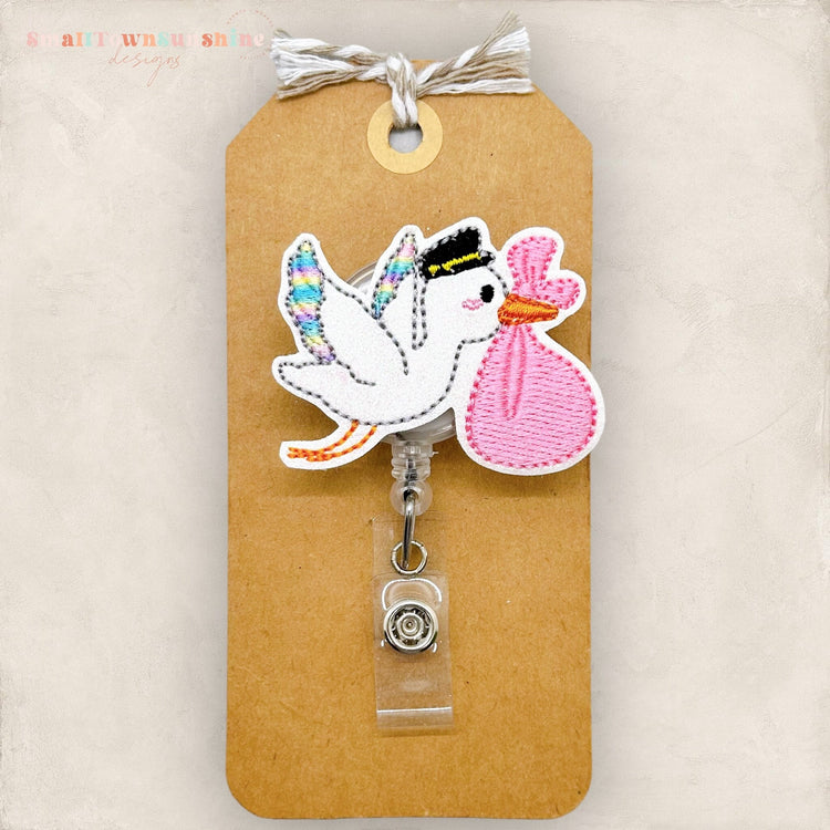pastel rainbow stork holding a pink swaddled blanket badge reel