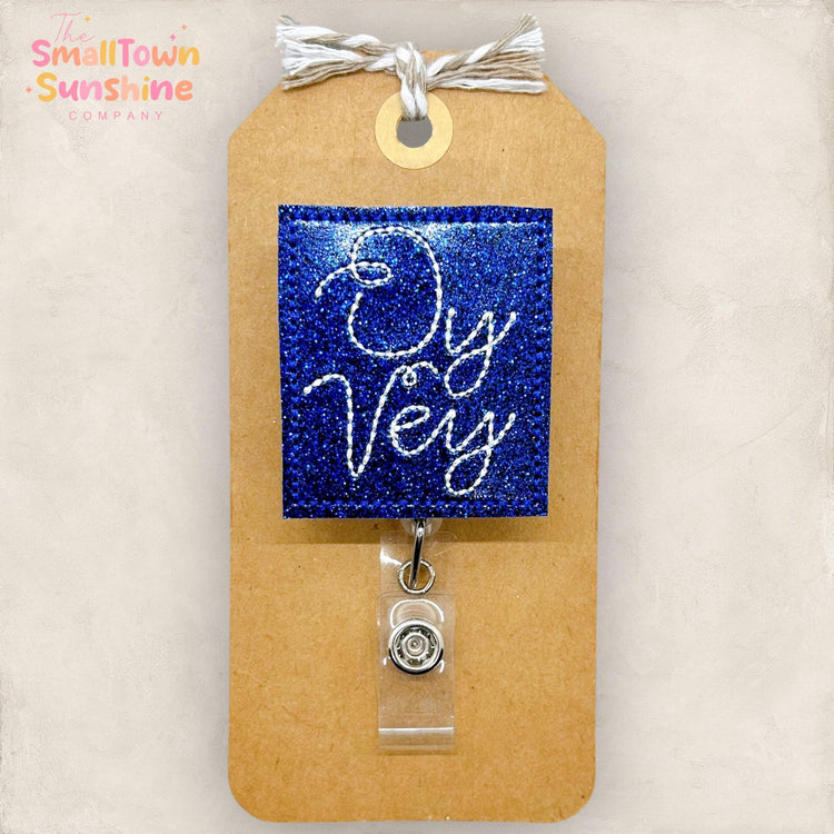 blue glitter vinyl embroidered badge reel topper with the words oy vey