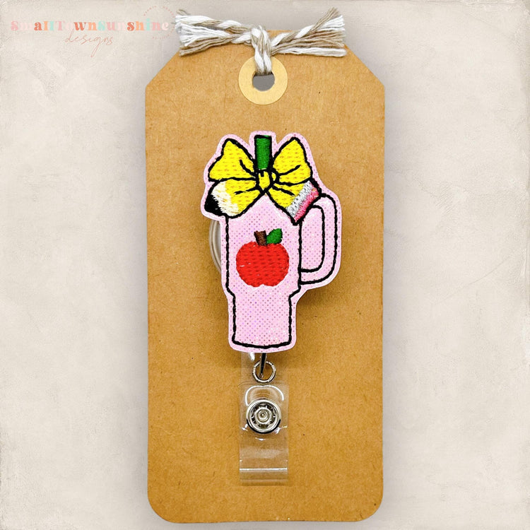 pink tumbler with apple and pencil bow badge reel