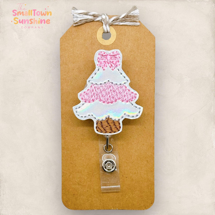 pink and white embroidered christmas tree with a bow badge reel topper