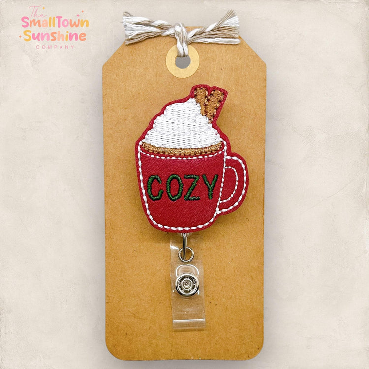 burgundy mug with the word cozy, mug with whipped cream and cinnamon sticks embroidered badge reel topper