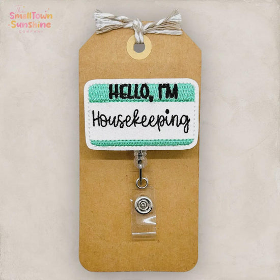 a brown paper tag with a green and white embroidered name tag attached to it. The name tag says "Hello, I'm Housekeeping".