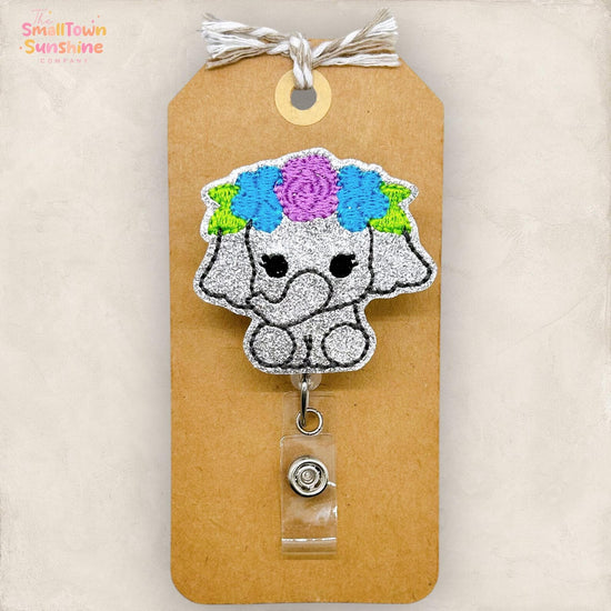 a small, glittery elephant-shaped badge with a floral headpiece attached to a brown paper tag.