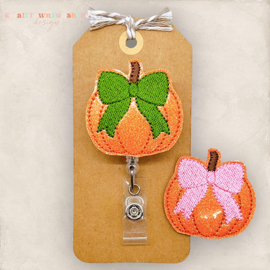 orange glitter vinyl pumpkin with embroidered coquette bow in green or pink badge reel topper