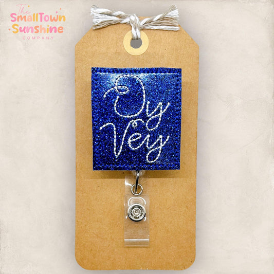 blue glitter vinyl embroidered badge reel topper with the words oy vey